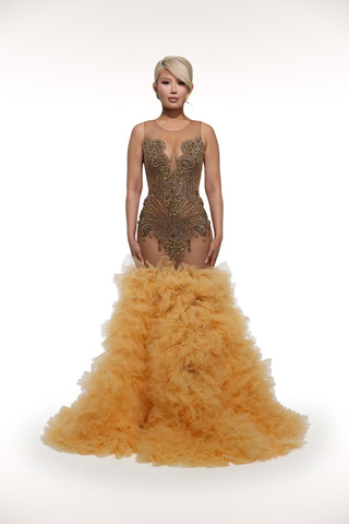 Woman wearing a gold evening gown with feathered skirt on a white background
